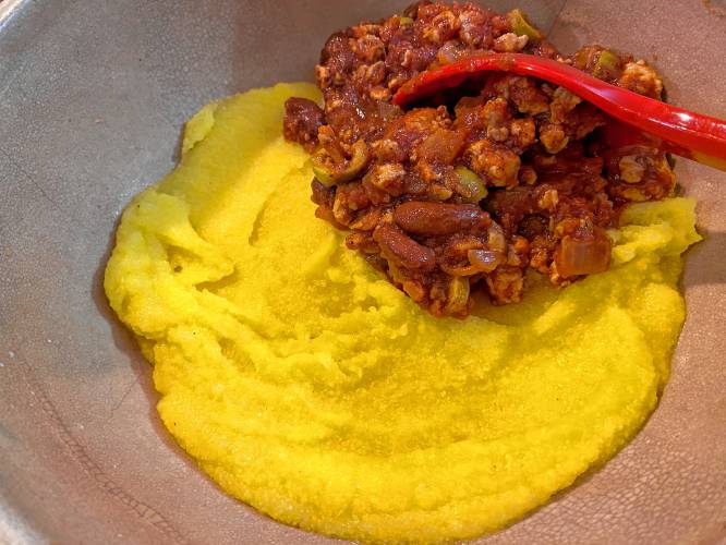 Spooning chili onto the cornmeal, prior to baking the casserole.