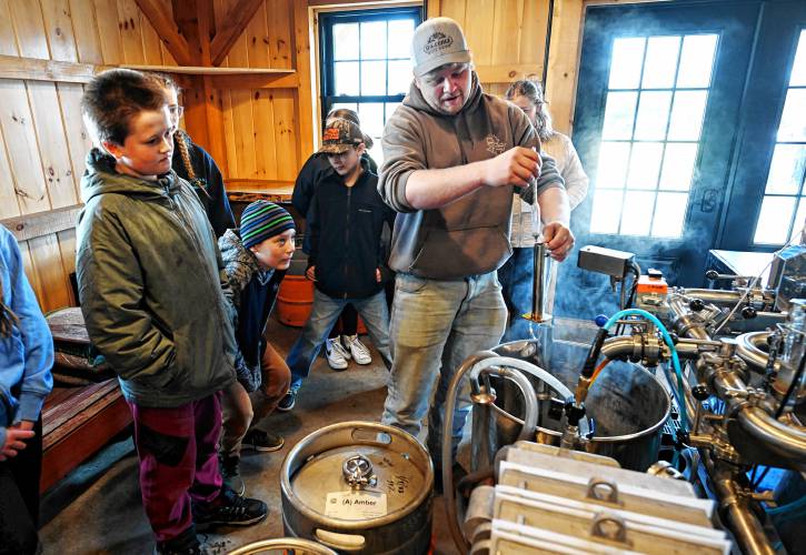 Jordan DiGeorge of Bald Mountain Sugar House in Bernardston checks the quality of the syrup he is drawing off his evaporator during a visit from students in Rory Flynn’s fifth grade class at Bernardston Elementary School on Friday.