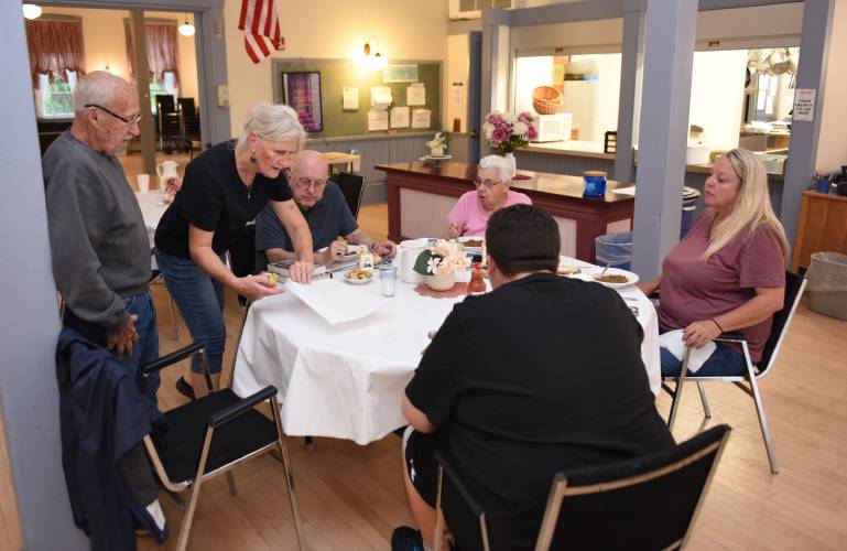 Clare Maguire, in black, sets a place for a meal at the Bernardston Senior Center in 2022. The Senior Center invites members to a Spring Lunch with Chef Clare on Wednesday, April 24, at 11:45 a.m. The lunch will include broccoli and cheese stuffed chicken, potatoes with sour cream and chives, spring blend vegetables, snowflake rolls and carrot cake.