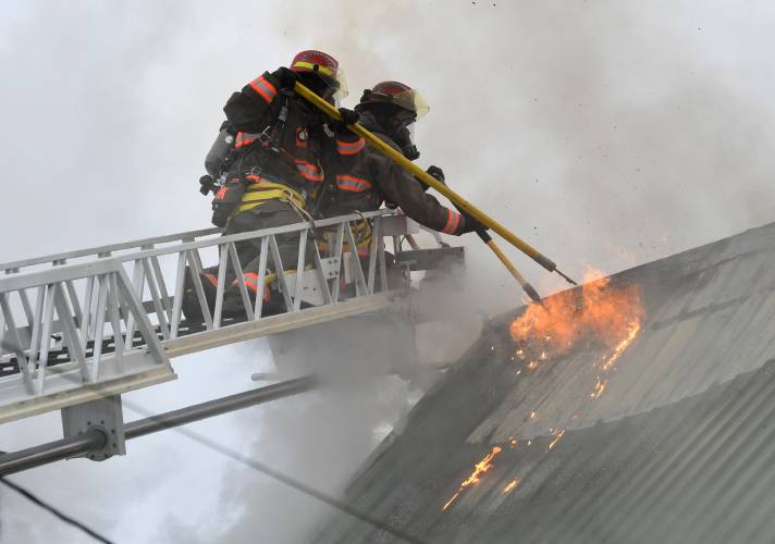 Firefighters on a North Adams ladder truck tear open a hole in the roof to ventilate a structure fire at 117 Readsboro Road in Monroe on Wednesday. 