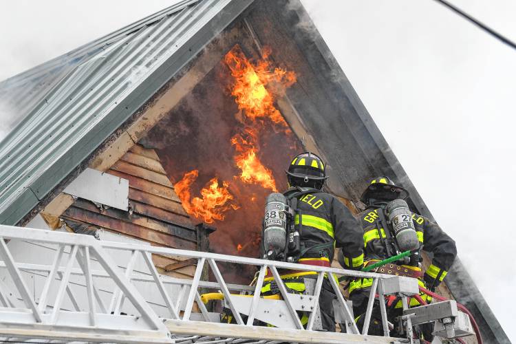 Greenfield firefighters on a North Adams ladder truck use a power saw and pike poles to ventilate a fire at 117 Readsboro Road in Monroe on Wednesday.