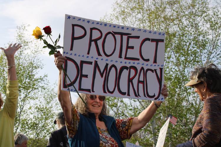 Helen Gibson Uguccioni holds her sign “Protect Democracy” with roses in hand at the “International Labor Day Bread and Roses Parade and Rally” in Turners Falls on Thursday.