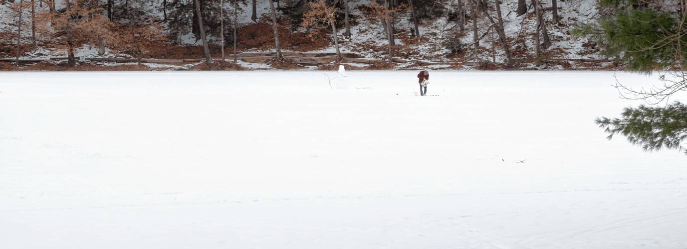 An ice fisherman walks on Puffer’s Pond in Amherst. Public safety officials warn residents to never trust ice over a body of moving water — one that has a flow or current.