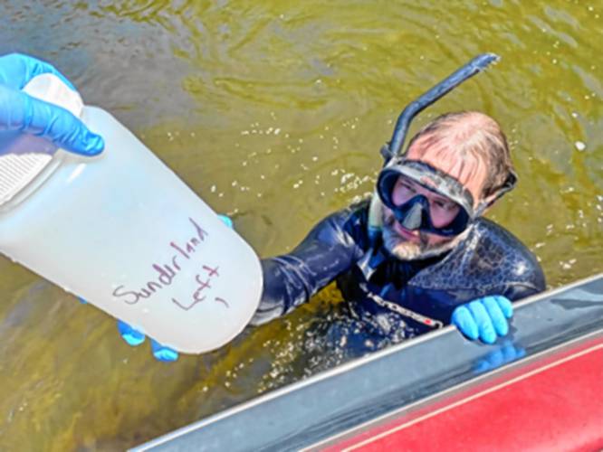 University of Massachusetts Amherst PhD candidate James Garner hands a collected water sample to a colleague on a boat in Connecticut River. 