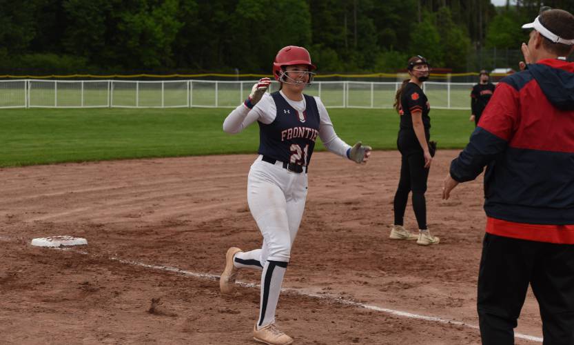 Frontier’s Raine Wonsey (21) rounds third base and high fives head coach Gary Deane after she blasted a solo home run over the left-field fence during the Redhawks’ game with South Hadley on Monday afternoon in South Deerfield.