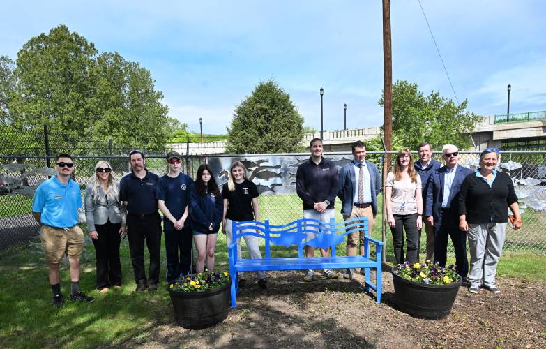 Franklin County Technical School students and faculty, local officials and representatives of FirstLight Hydro Generating Co. take a group photo celebrating the bench and aluminum fish silhouettes made by Franklin Tech for the courtyard at the Turners Falls Fishway near the dam.