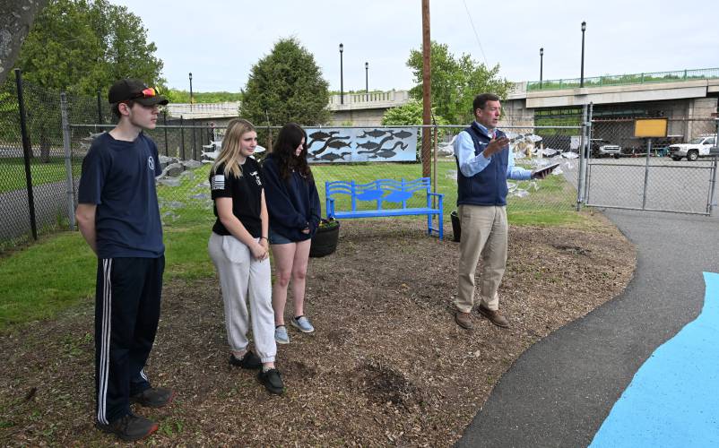 Andy Brydges, director of community relations at FirstLight Hydro Generating Co., at right, speaks to those in attendance at the Turners Falls Fishway for the reveal of the metal artwork and a bench created by students at Franklin County Technical School. From left, the students are Brandon Janik, Jenna Petrowicz and Lilliana Lonergan.