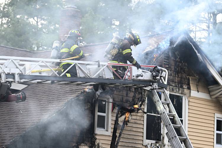 Firefighters pick at a burning eve at a house fire at 41 Rogers Ave. in Orange on Sunday afternoon.