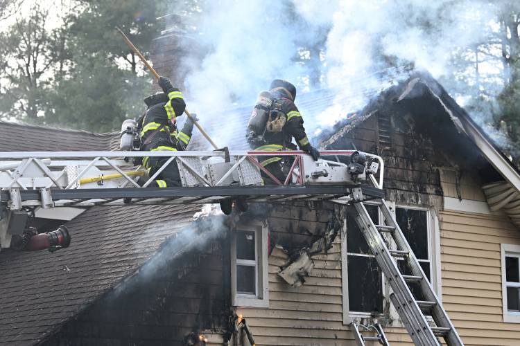 Firefighters pick at a burning eve at a house fire at 41 Rogers Ave. in Orange on Sunday afternoon.