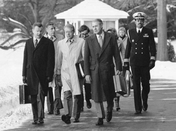 President Jimmy Carter, flanked by Secretary of State Cyrus Vance, right, and foreign policy adviser Zbigniew Brzezinski, left, walks toward a waiting helicopter to fly to nearby Andrews Air Force Base, Md., on the South Lawn of the White House in Washington, Feb. 14, 1979.