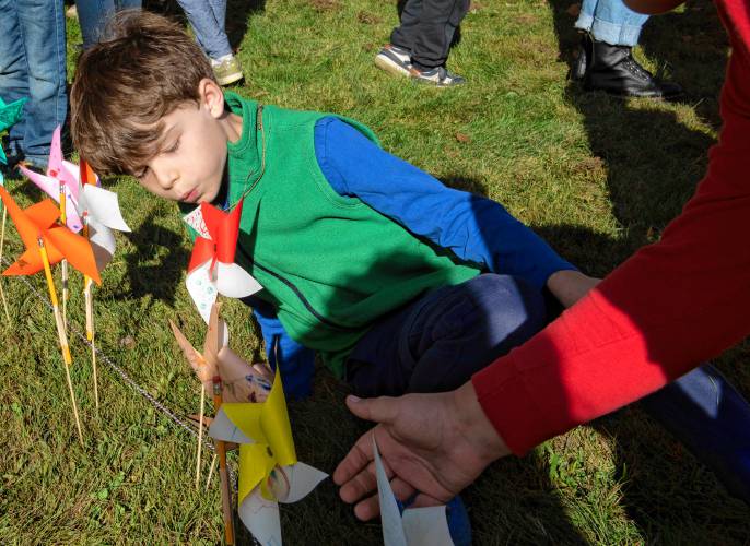 Arlo Mandel, a second grader at Leverett Elementary School, blows on a pinwheel placed on the border of a large peace sign at the school.