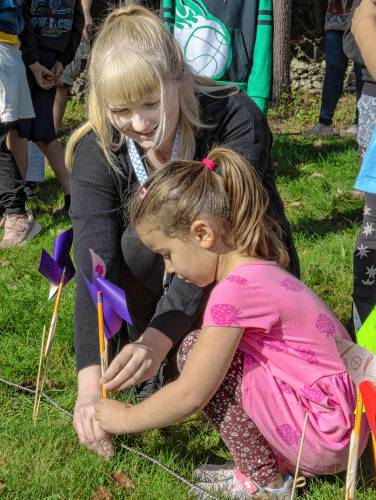 Michaela Kelly, a kindergarten teacher, helps Susie Hicks, a kindergartner at Leverett Elementary School, place a pinwheel on the borders of a large peace sign as a way to celebrate International Peace Day on Tuesday.