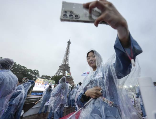 Asom Kim, a physiotherapist from team South Korea takes a selfie with the Eiffel Tower from a boat down the Seine River in Paris, France, during the opening ceremony of the 2024 Summer Olympics, Friday, July 26, 2024. (AP Photo/Lee Jin-man, Pool)
