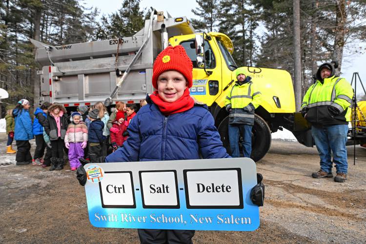 Swift River School kindergartner Teddy Koonz holds a placard for the school with his winning suggestion for the name of a snowplow, “Control-Salt-Delete.” At right is Michael Lovett of the state Department of Transportation, who will be driving the 2024 Freightliner out of Bernardston.