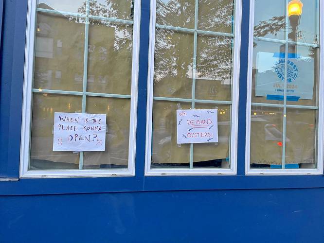 This photo shared on X by Only in Amherst in July 2024 shows signs posted to the windows of the Amherst Oyster Bar reading “when is this place gonna open?” and “we demand oysters!”