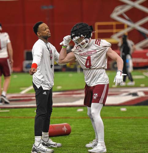UMass wide receivers coach Jordan Hogan, left, demonstrates a drill with Sterling Galban, right, to the rest of the receiver group during the Minutemen’s first football practice of the spring season on Monday morning in Amherst.