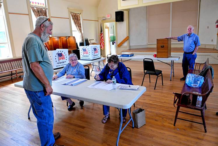 Warwick resident Brian Gale is checked in to vote in Warwick Town Hall by Gloria Varno and Dawn Magi while Constable George Day waits to tally his ballot on Monday. 