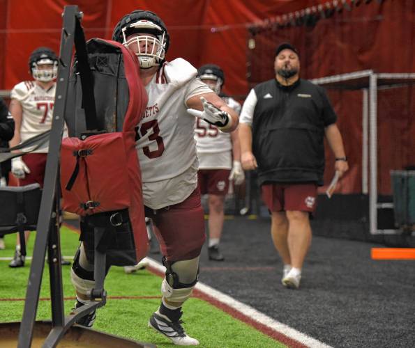 UMass offensive lineman Brock Taylor (73) participates in a blocking drill while offensive line coach Kurt Anderson, back, looks on during the Minutemen’s first football practice of the spring season on Monday morning in Amherst.