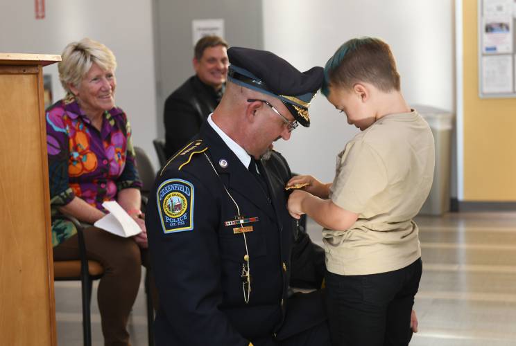 Greenfield Mayor Ginny Desorgher looks on as Todd Dodge’s grandson Silas Dodge, 6, pins his badge on after he was sworn in as Greenfield’s permanent police chief during a ceremony at the John Zon Community Center on Tuesday evening.