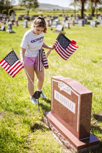 Greenfield High School Student Council member April Rooney-Adams puts out flags for veterans at Calvary Cemetery on Saturday, May 11.