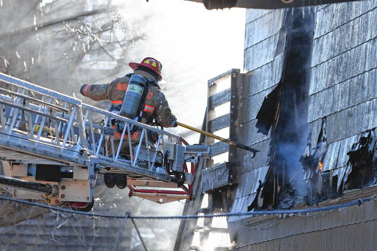 A firefighter on Northfield Fire Department’s ladder truck ventilates the building by breaking a window at a fire Sunday morning at 75 School St. in Greenfield.