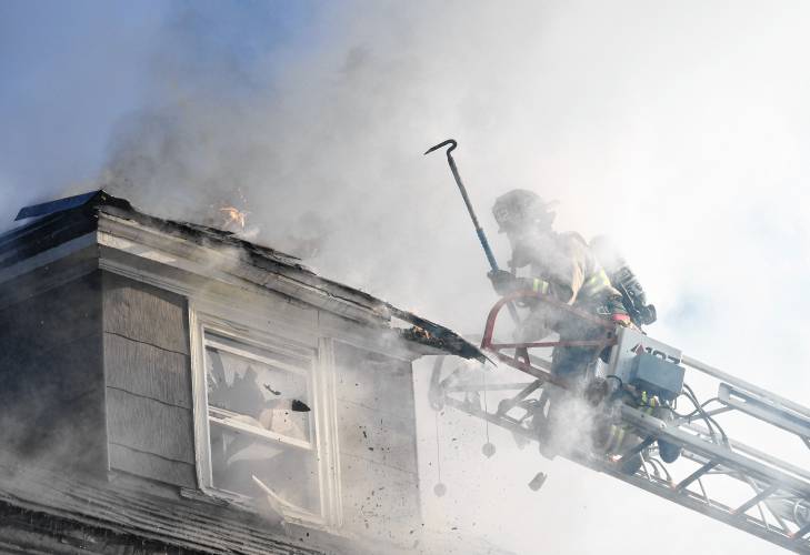 Turners Falls Firefighter William Doyle uses a Boston Rake to pull apart a burning dormer at a fire Sunday morning at 75 School St. in Greenfield.