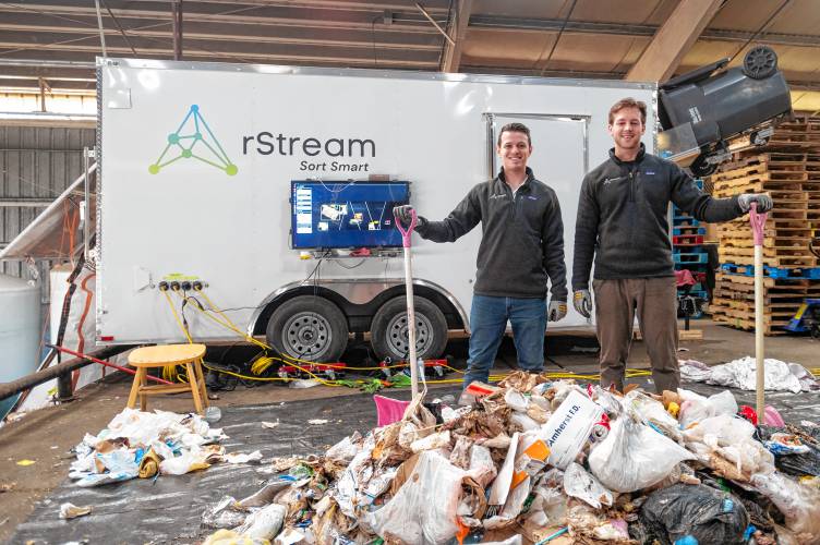 rStream co-founders Ian Goodine, left, and Ethan Walko stand beside their trash sorter at the UMass Waste Recovery and Transfer Facility in Amherst. The mechanism within the trailer uses artificial intelligence to sort trash and recyclables.