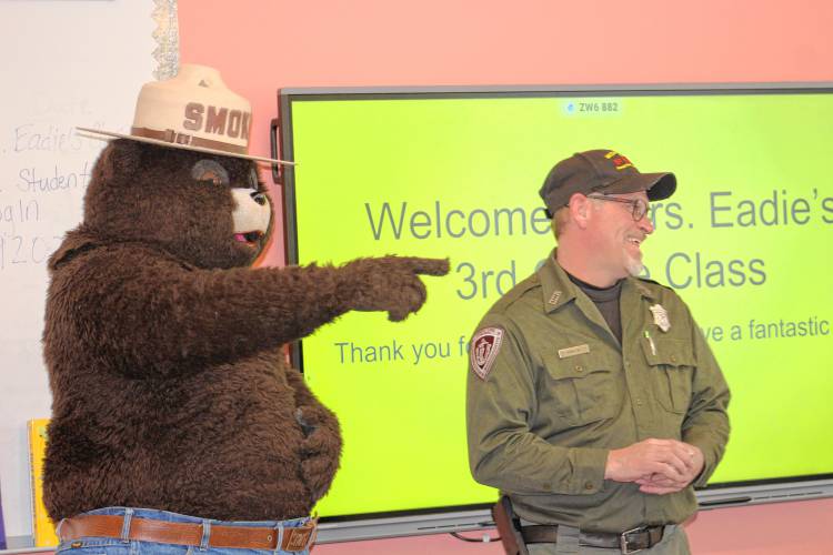 Smokey Bear and Herman Meattey, forest fire patrolman at the state Bureau of Forest Fire Control and Forestry’s location at Erving State Forest, speak with students during their visit to Fisher Hill Elementary School in Orange on Tuesday as part of Read Across America.