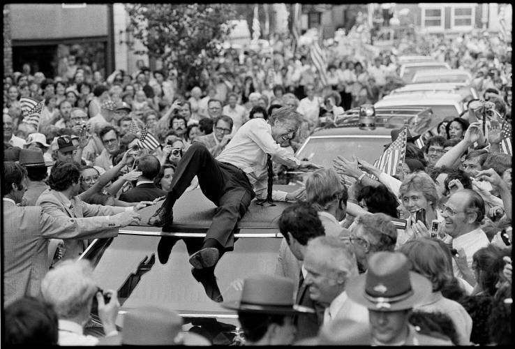 President Jimmy Carter leans across the roof of his car to shake hands along the parade route through Bardstown, Kentucky, on July 31, 1979. The president climbed on top of the car as the parade moved toward the high school gym, where a town meeting was held.