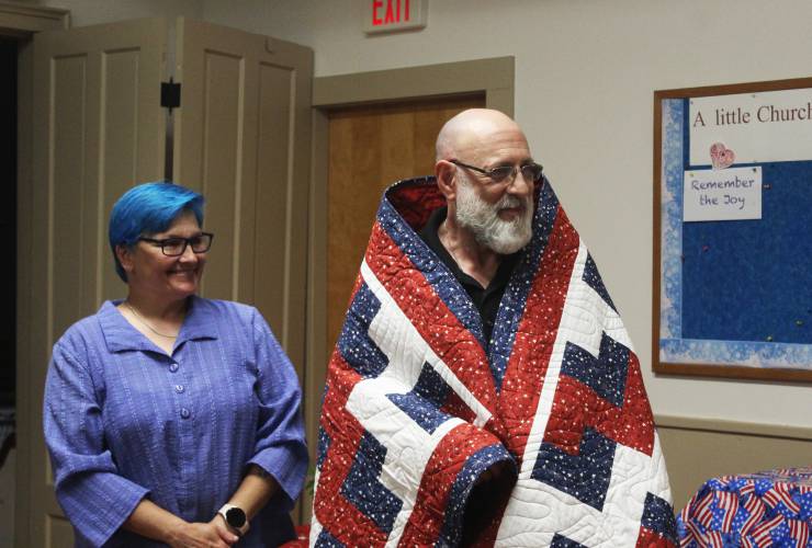 U.S. Navy veteran Kenneth Chaisson smiles while wrapped in a Quilt of Valor he received from the North Orange Grange during a ceremony at the Community Church of North Orange and Tully on Tuesday, as his wife, Traci Beroldi, stands to his right.