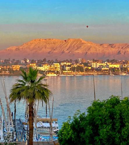 Looking across the Nile River to an Egyptian city and a background of sand dunes.