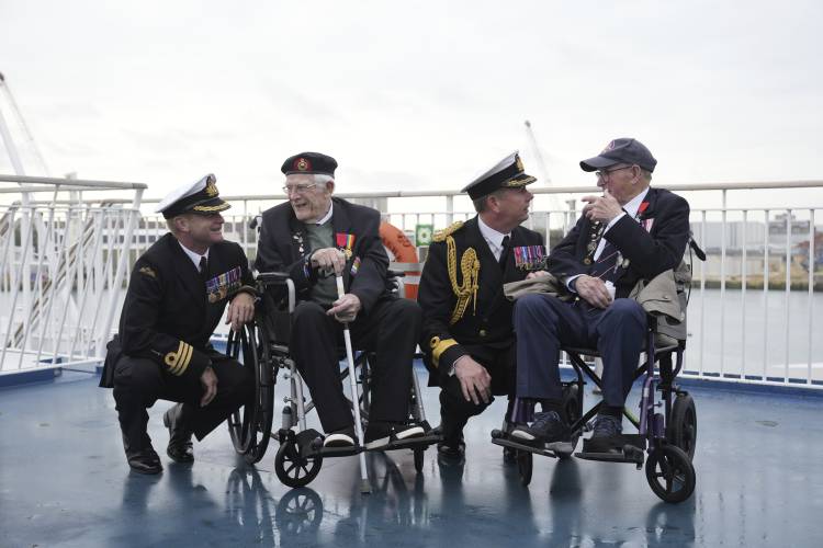 British Normandy veterans Jim Grant, second left and Charles Horn, right pose with British Royal Navy officers Commander Glen Hinson, left and Commodore John Boyce on board the Mont St Michael ferry prior to departure for France, in Portsmouth, England, Tuesday, June 4, 2024.