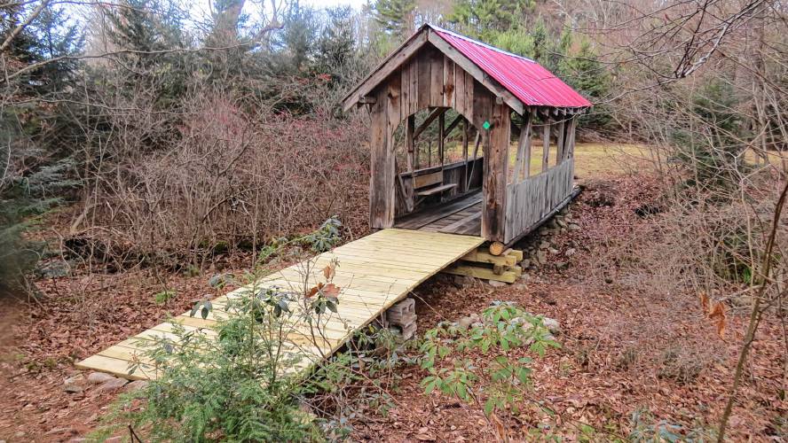A covered bridge at the Blueberry Patch in Leverett, featuring a memorial bench and plaque for late landowner Gordon King.