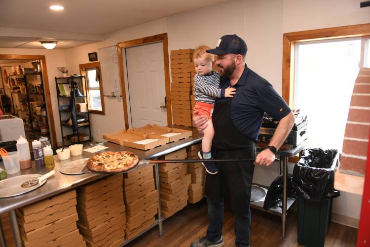 Jon Flis with Jack, 2, takes a pizza out of the wood-fired pizza oven at Flis Market in Erving.