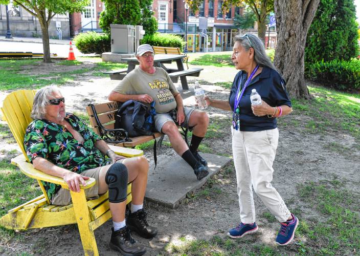 Maria Burge, right, the new community liaison for the Greenfield Police Department, offers water to Greenfield residents Jim Grant and Shawn LaBier on the Greenfield Common on Friday.