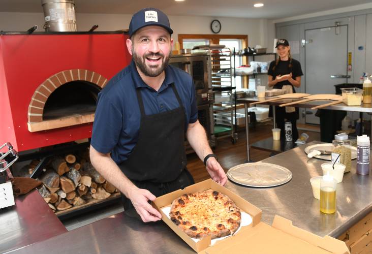 Jon Flis boxes up a wood-fired pizza, with Coco King tossing dough in the background, at Flis Market in Erving.