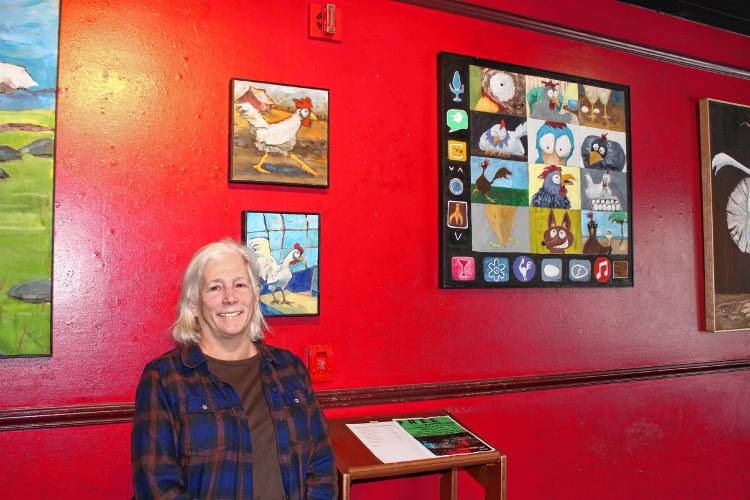 Pat Little poses in front of some of the paintings in her “Cosmic Chickens” series, currently on display at Mocha Maya’s in Shelburne Falls.