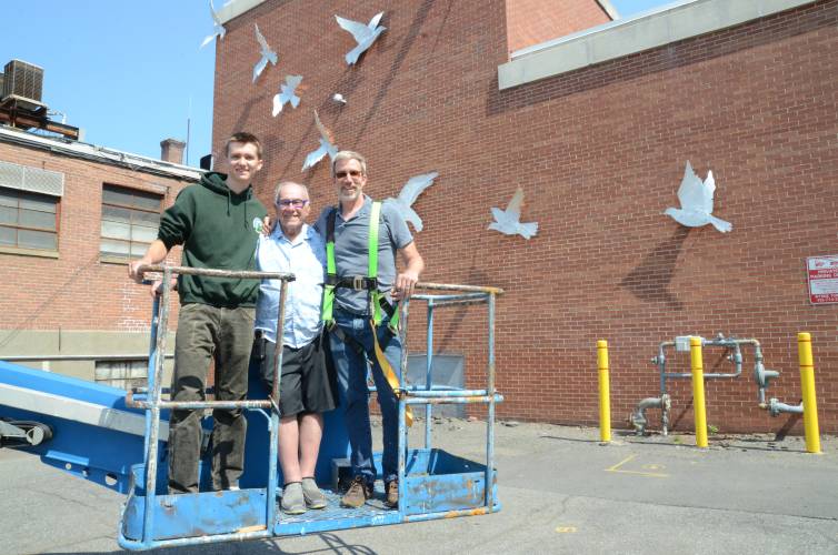 Three generations of Zaccheos — from left, Gabe, Tom and Mark — stand next to the “Flight of Fancy” mural  that was conceptualized and fabricated by Tom Zaccheo at the Greenfield Recorder’s 14 Hope St. building, owned by his son Mark, in June 2023. The elder Zaccheo is opening his next art exhibit, “Transformed by Fire: Feats of Clay,” in Connecticut on Sept. 5.