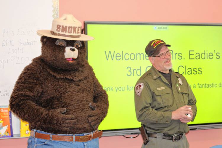 Smokey Bear and Herman Meattey, forest fire patrolman at the state Bureau of Forest Fire Control and Forestry’s location at Erving State Forest, speak with students at Fisher Hill Elementary School in Orange on Tuesday. The students received gift bags filled with an activity book, copies of Smokey Bear’s origin story, rulers, pencils, erasers and coloring books.